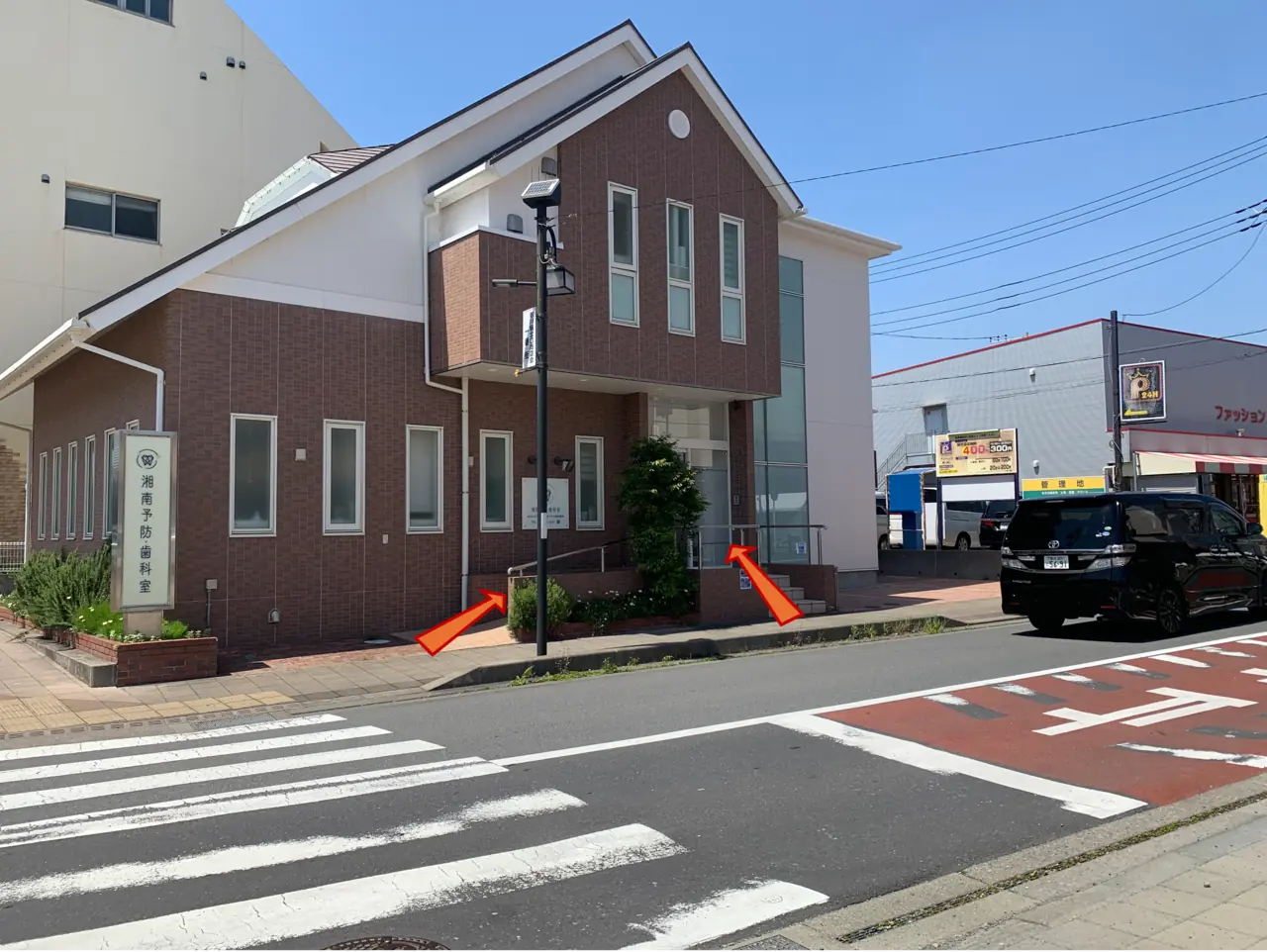 湘南予防・歯科室の看板が見えます。横断歩道を渡った先が入口です。スロープと階段があります。